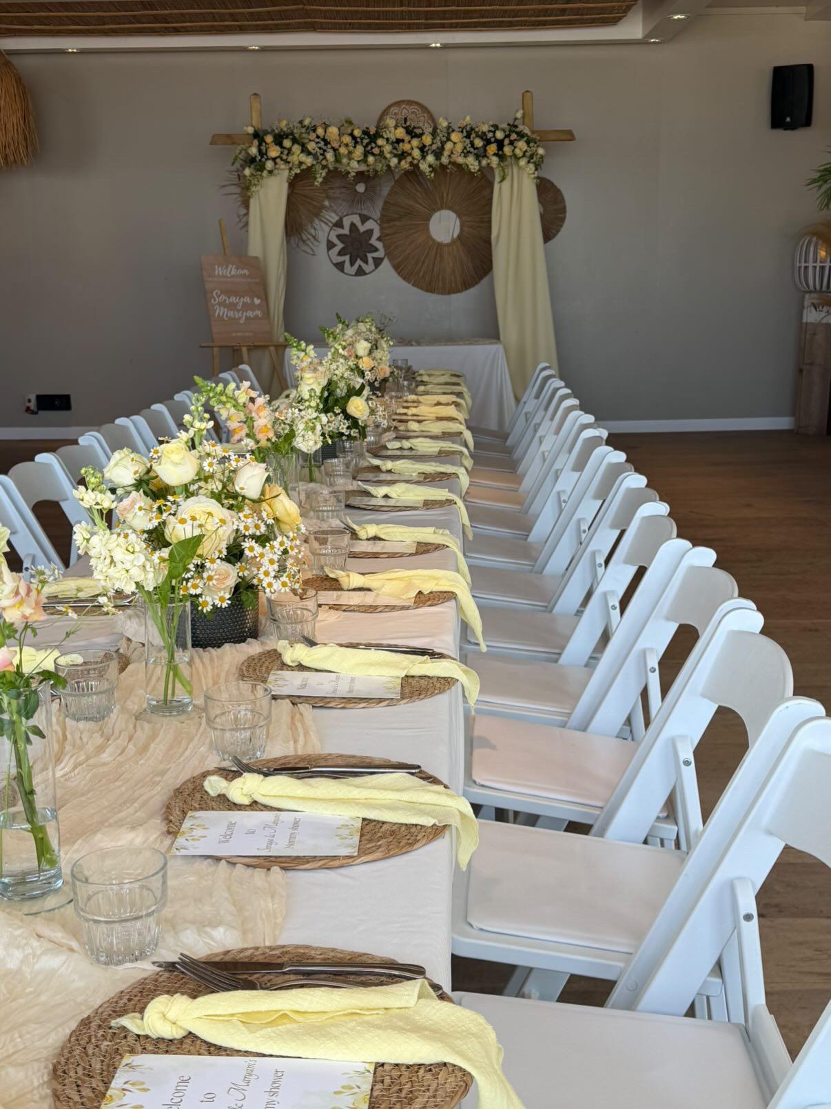 Lange gedekte tafel met bloemenboog tijdens een babyshower aan zee bij Zeezicht